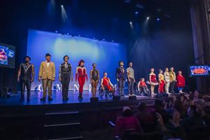 Performers from various backgrounds, some using wheelchairs, stand together under bright stage lights. Their colorful costumes and confident postures convey pride and belonging, celebrating diversity and inclusion within the performing arts.