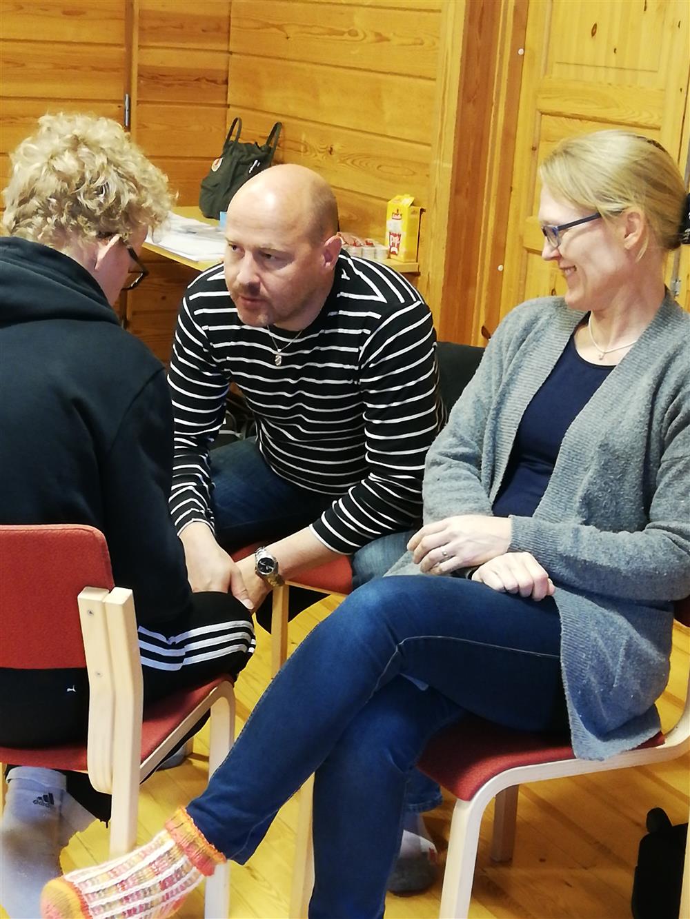 A family sits in a circle at the local On the Verge of Adulthood workshop, smiling and watching each other.