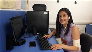 A young woman sits at a computer with her hands on the keyboard. Her head is turned slightly to smile at the camera.
