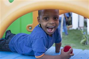 A young boy laughs, while holding a ball and playing outside on the playground of INAIPI centres.