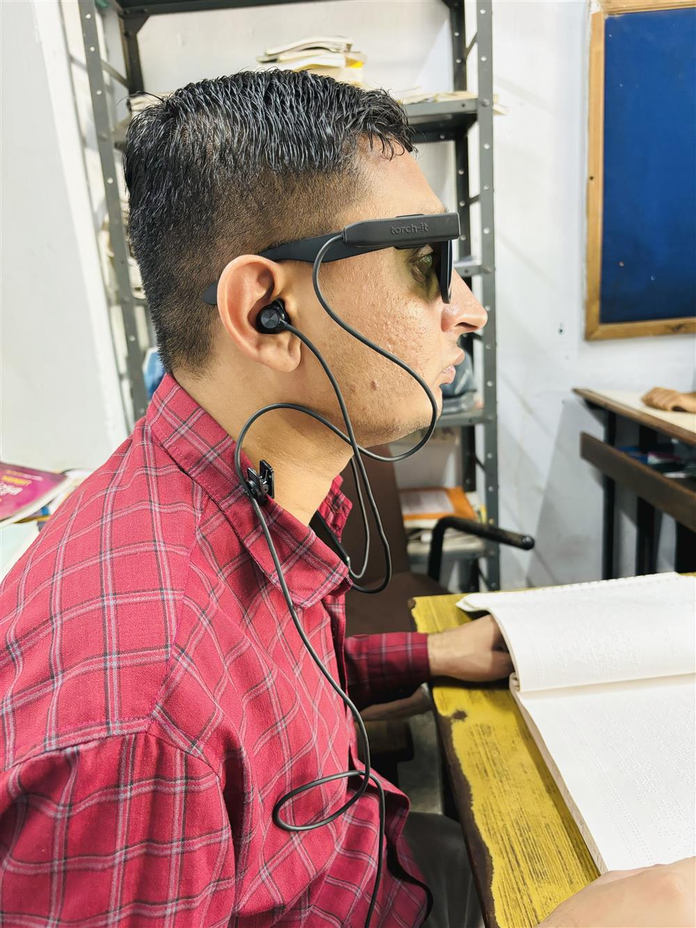 An Asian man reads a Braille book while wearing smart glasses with audio support. This innovative technology enhances accessibility for people with visual impairments, reflecting dignity, autonomy, and the transformative power of inclusive design.