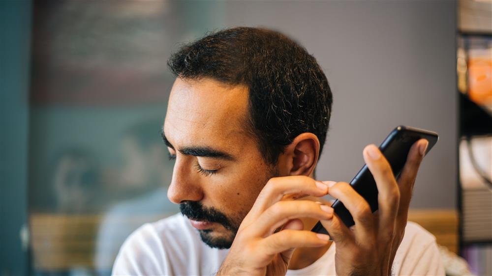 A man, possibly with visual impairment, uses a smartphone through touch and audio features. The photo conveys dignity and independence, showing how accessible technology empowers people to connect, learn, and participate equally in the digital era.