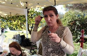 A woman under a tent looks to the right while putting on mascara. 
