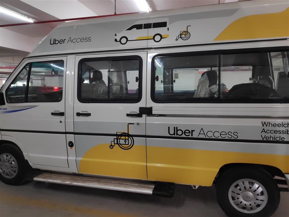 This photo shows a silver and white accessible minivan parked in a garage. Written on the side of the van is the lettering "Uber Access" next to a symbol of a wheelchair. 