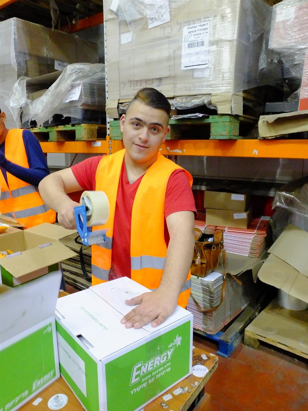 A young man is packing boxes during his job training in the warehouse in front of full shelves.