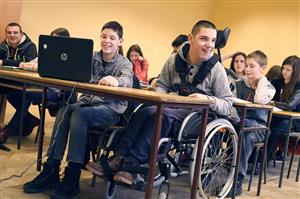A boy sits in the front row in a wheel chair, learning together with other children in the background in a classroom.