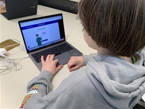 A boy in hoodie looking at his computer. In his screen is an animation of a boy and a pair of socks with a banner "Det här är Milo".