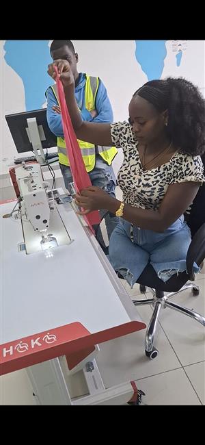 A young African woman attentively sews fabric using an accessible sewing machine while a man observes nearby. The scene reflects empowerment through vocational training and the importance of inclusive employment opportunities that value skill and independence.