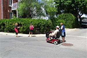 A person on a wheelchair and three other people crossing a wide road.
