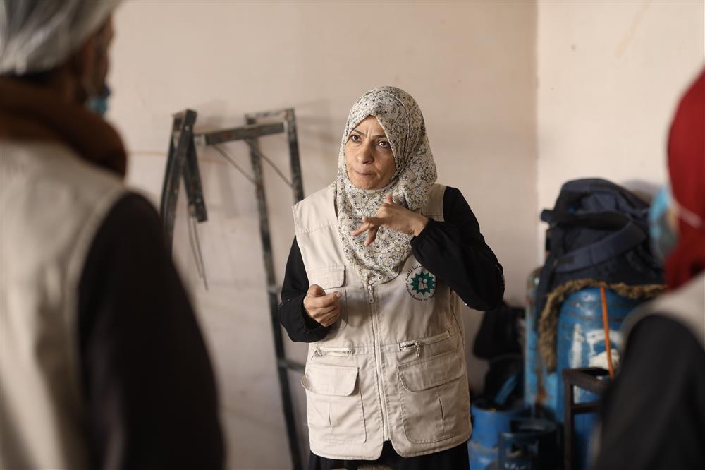 A Middle Eastern woman wearing a headscarf speaks expressively with her hands while communicating with colleagues. Her confident presence highlights the power of women’s leadership and inclusion in humanitarian work, bridging understanding across communities with empathy and respect.