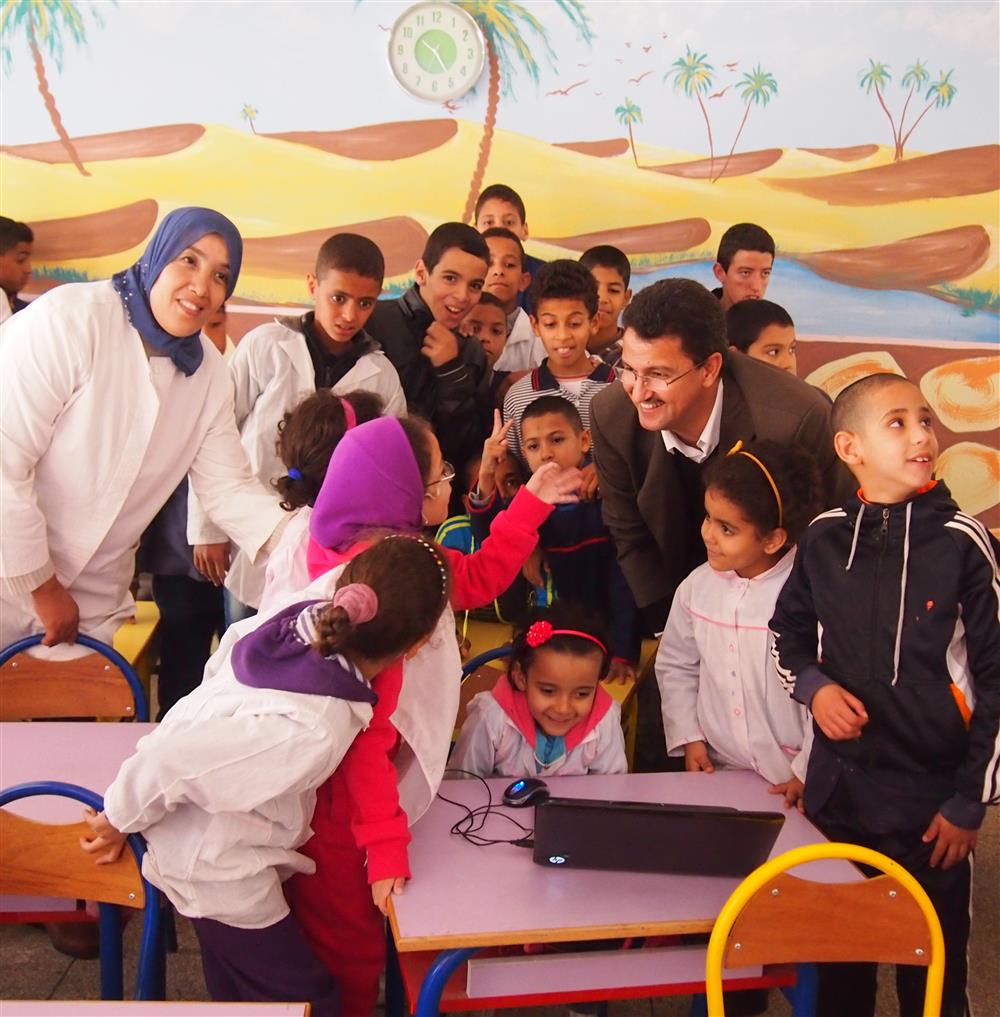 A group of children in the classroom watching something projected on the laptop.