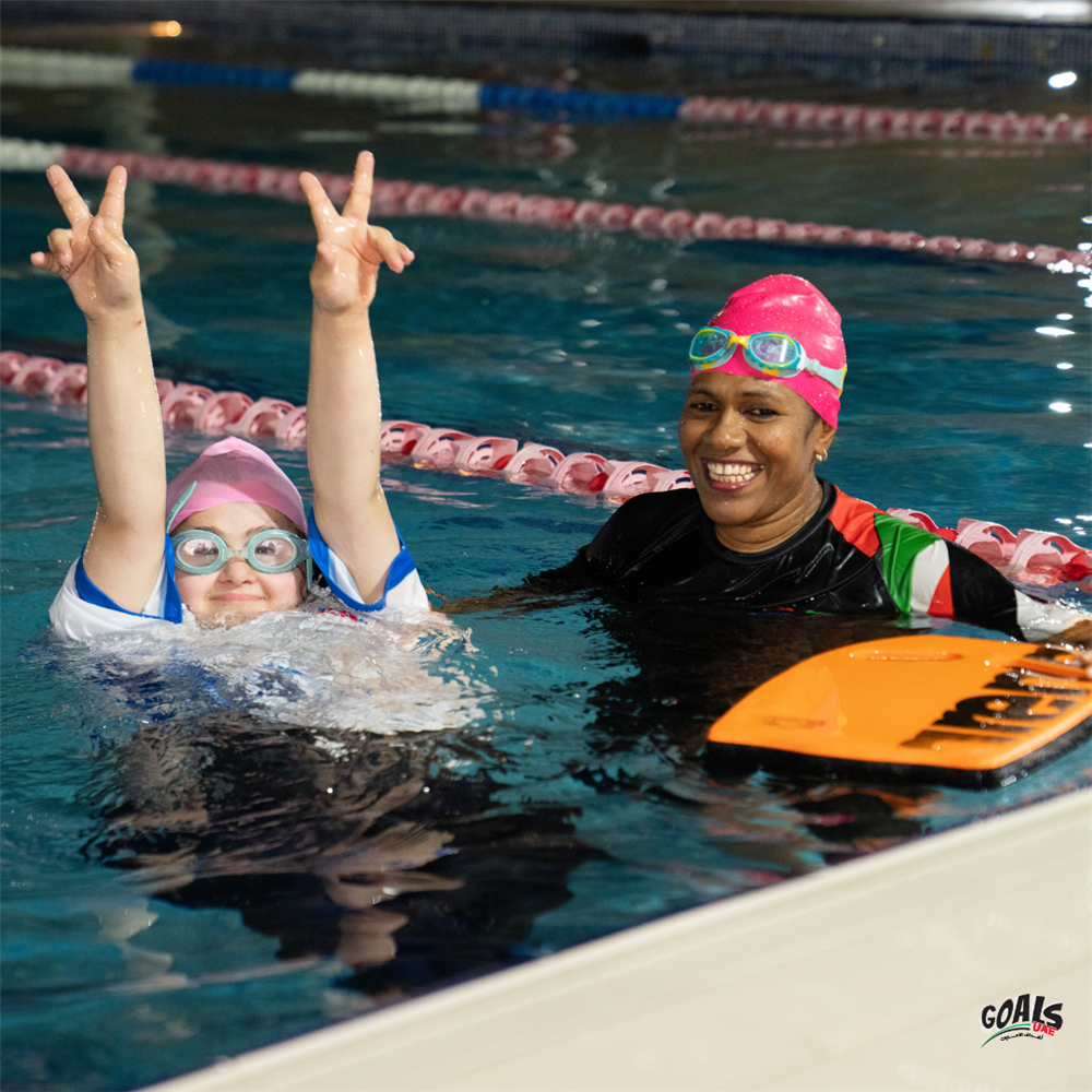 Two swimmers, one with Down syndrome and her instructor, share a joyful moment in the pool. Their expressions of confidence and teamwork show how inclusive sports foster equality, health, and belonging through shared effort and encouragement.