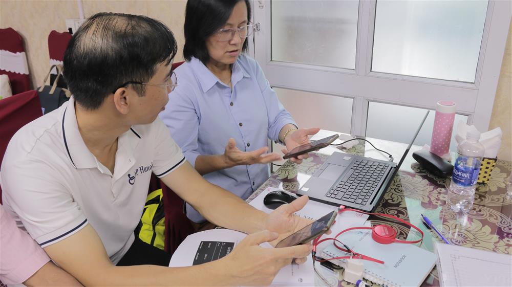 Two people are seated at a table, using their smartphones and a laptop while discussing something attentively. Their collaboration reflects digital inclusion and shared learning, emphasizing the importance of accessible technology for communication and education.