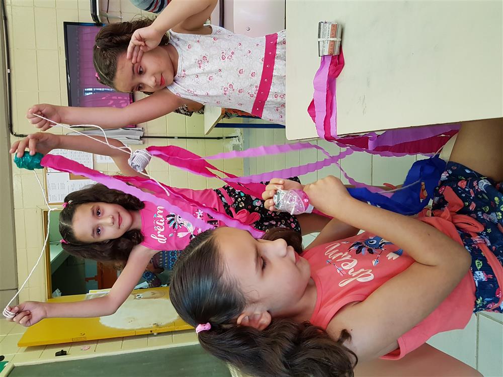 Three girls, Lara in the front and her twin sister and another girl in the back, are playing with pink ribbon.