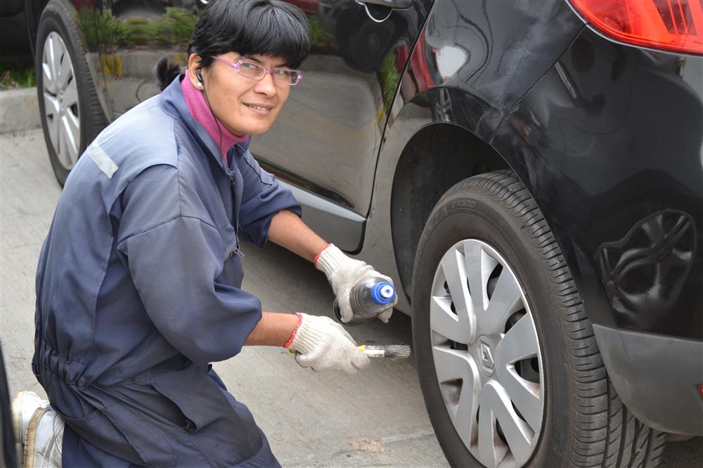 A lady is cleaning a tire of a car. She has some cleaning material and a brush in her hand. She is wearing head phones.