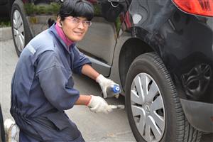 A lady is cleaning a tire of a car. She has some cleaning material and a brush in her hand. She is wearing head phones.