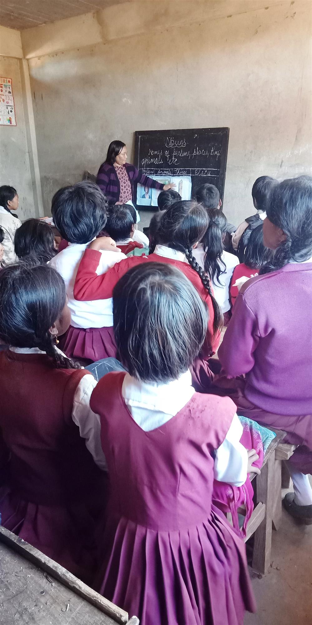 Girls in violet uniforms sit in several rows in front of the blackboard during class.