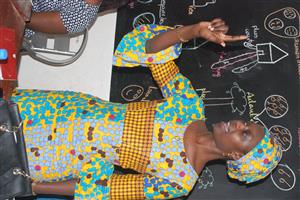 A colorful dressed woman is teaching sign language in front of a blackboard with drawings at the Teacher's training class.