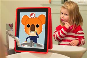 An animated bear with a countdown timer played on an iPad next to the faucet while a preschooler girl wearing a striped pullover is standing in front of the basin and a mirror brushing her teeth. 