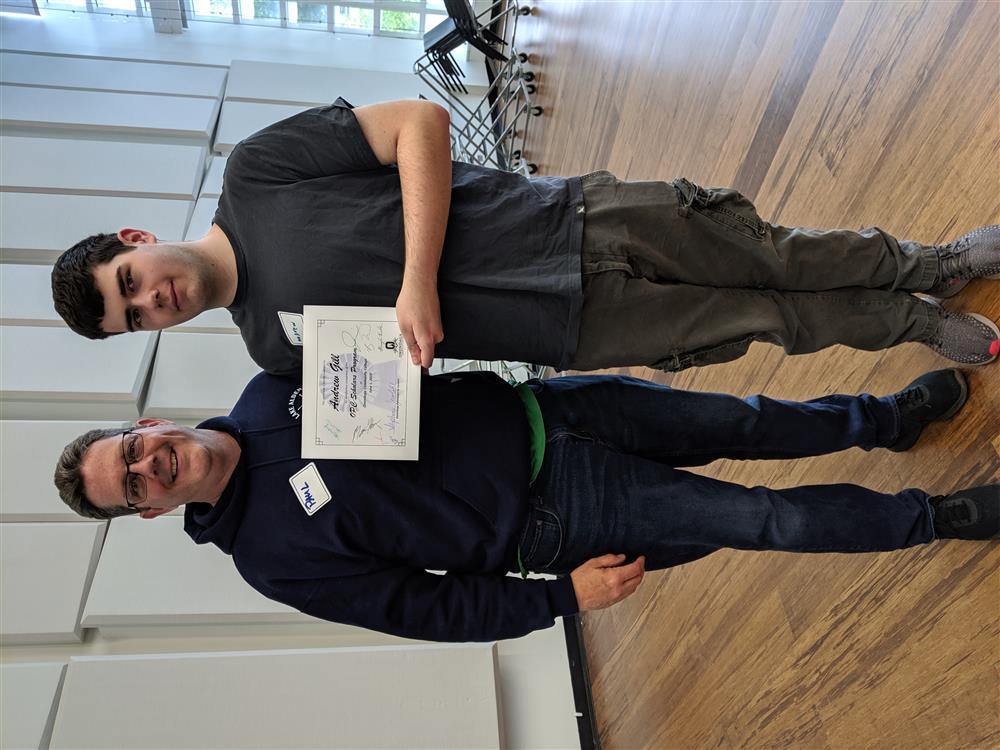 A graduate holds his graduation certificate next to his teacher.