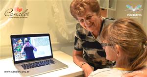A old lady grins at a girl, who is watching a video on her laptop.