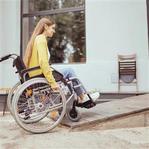 A young woman in a wheelchair moves confidently up a ramp outside a building. The image represents accessibility and independence, highlighting how inclusive environments enable equal participation and mobility for everyone.