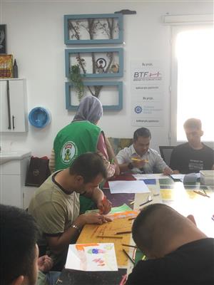 People engage in a creative workshop, drawing and coloring together in a welcoming classroom supported by local and international organizations. The image reflects inclusion and empowerment through art, fostering dignity and participation for people of all abilities.