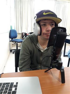 Man with head phones sits in front of microphone, recording for an online radio program.