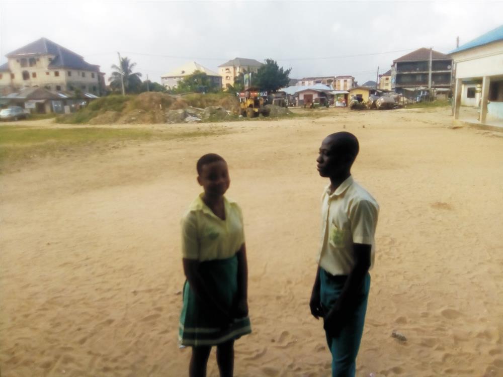 Two African students standing in a field. Buildings and houses are behind them in a significant distance.