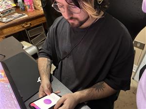 A young person wearing glasses and headphones uses a smartphone app at their desk. The scene conveys independence, digital literacy, and the value of assistive or accessible technology in promoting inclusion for all users.