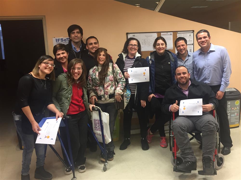 Young women and men, all of the with different disabilities have come together for a group picture. Some of them hold certificates into the camera. They are all smiling.