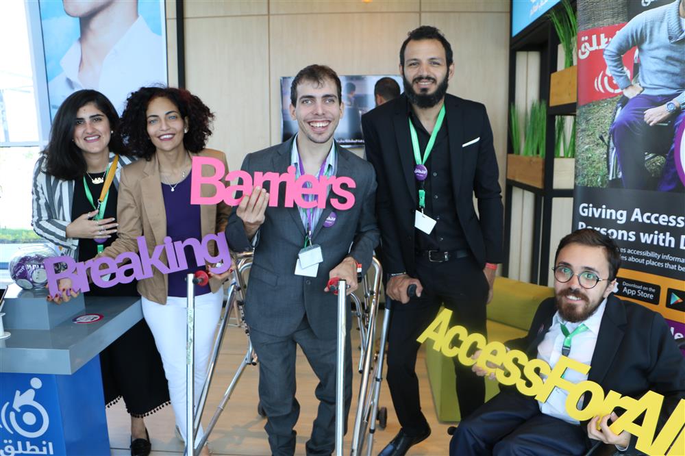 Five persons, two women and three men with different disabilities hold up signs saying: “Breaking barriers, access for all!” They are at a booth at the World Youth Forum in Sharm El-Sheikh.