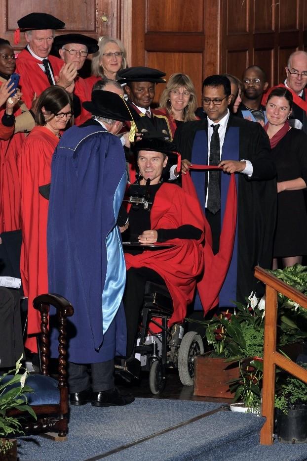 Vic, a project participant in a wheel chair graduats, while people in ropes are standing around him and smiling.