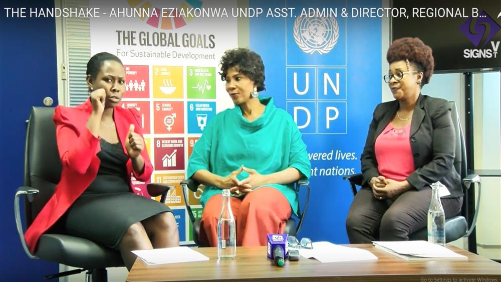 Three women sit, while having a discussion in sign language live on Signs TV in front of UN sustainable goals posters.