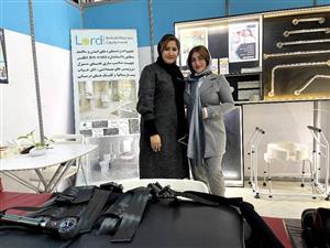 Two women stand together in a booth displaying rehabilitation and accessibility equipment. Their confident expressions and professional setting reflect innovation and leadership in inclusive design, advancing dignity and independence for people with disabilities.