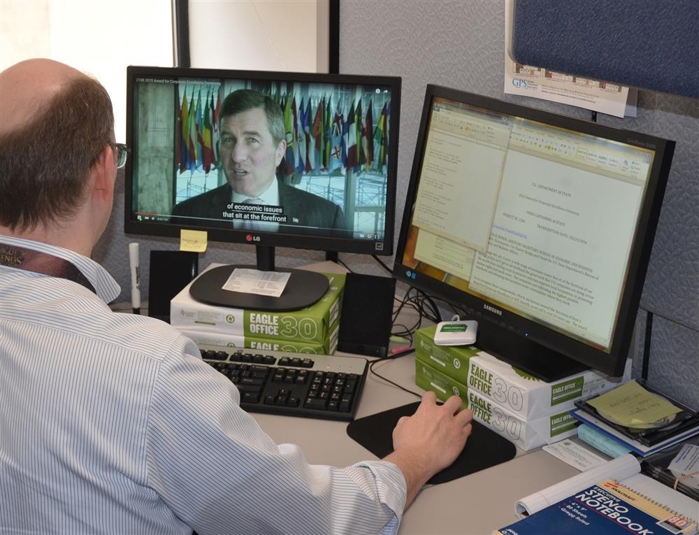 A man in the office watching a Youtube video on the PC with captions.