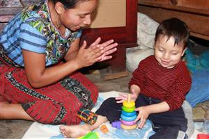 Mother claps her hands while her child is playing with toys attending early intervention therapy.