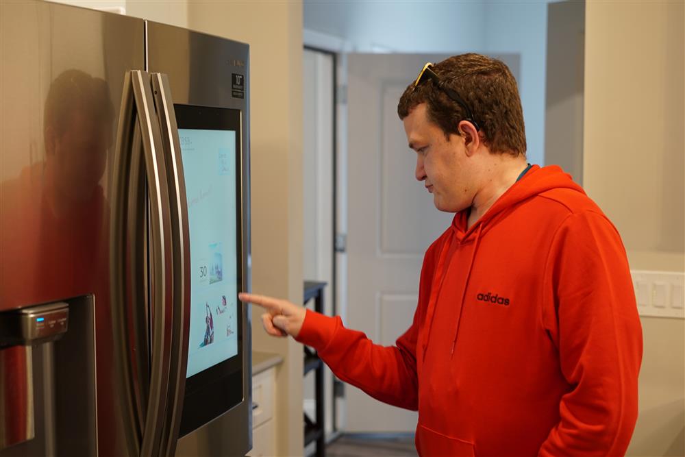 A man appearing to have an intellectual disability pointing on the digital screen of a two-door refrigerator.