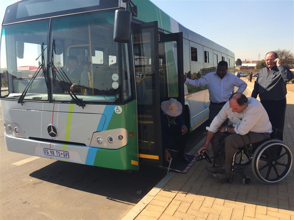 A man on the wheelchair inspecting the accessible features of a bus. 