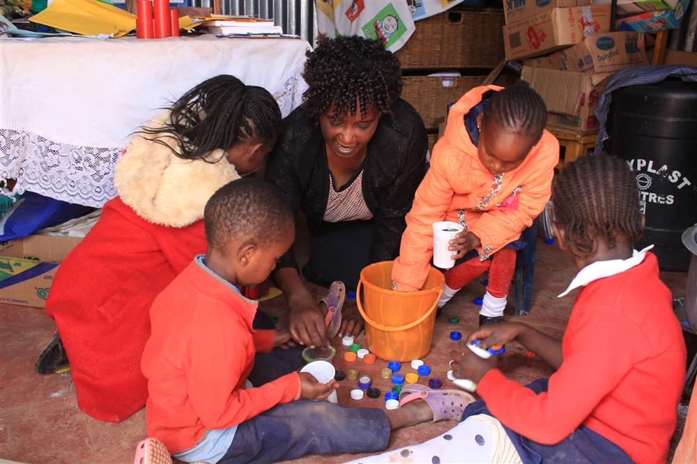 Teacher sits in a circle with her students, while teaching them with low cost learning materials like colorful buttons.