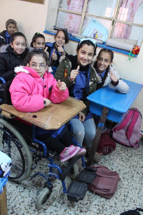 Tuleen, a project participant in a wheel chair with an attached desk, studys together with other children in a classroom.
