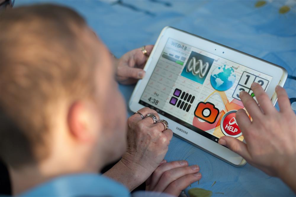 Person with disability accessibly the Big Red Button App on the tablet.