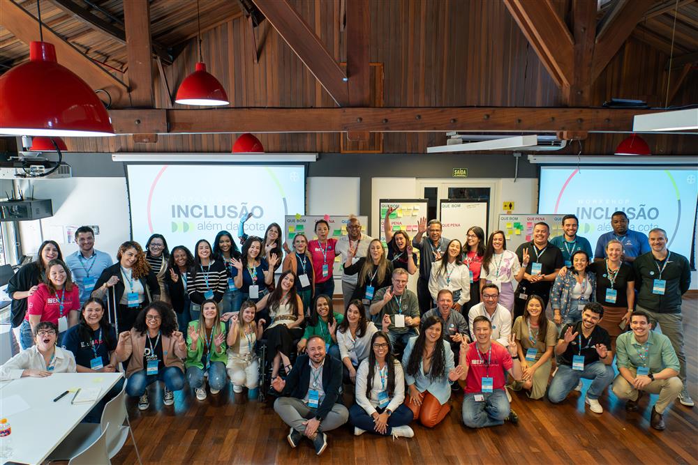 A diverse group of people smiling together during a workshop titled “Inclusão além da cota” (Inclusion beyond the quota). The participants are of different genders, backgrounds, and abilities, embodying unity and equality in an inclusive learning environment.
