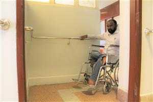 A man on a wheelchair entering a room with accessibility features to hold on to. 
