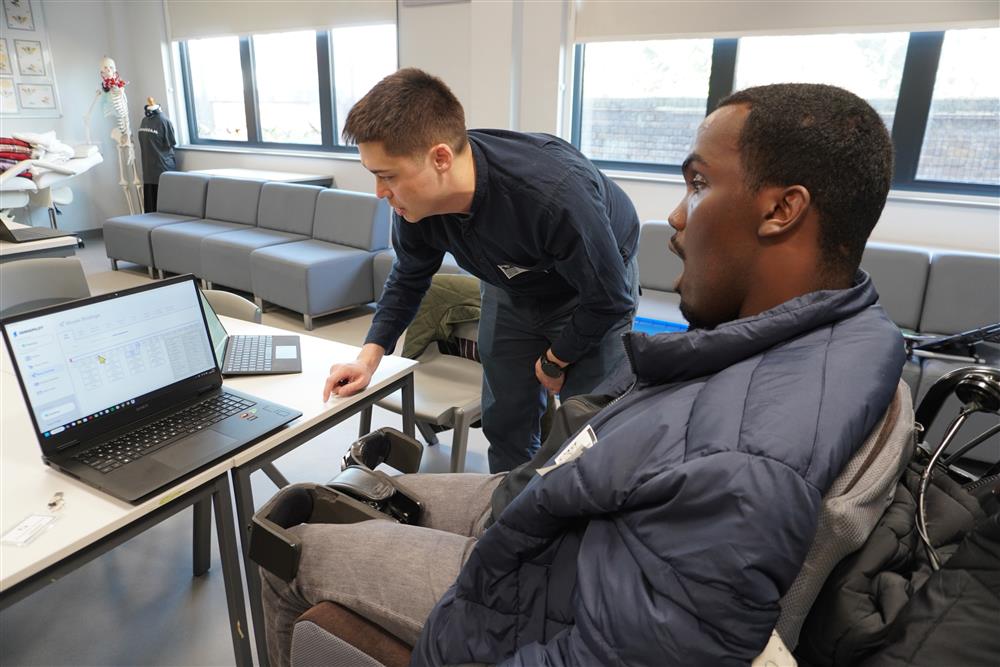 In a bright lab setting, a man in a wheelchair collaborates with another person at a computer. They appear to be testing adaptive technology, symbolizing innovation, teamwork, and how assistive design fosters independence and inclusion for people with disabilities.