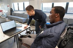 In a bright lab setting, a man in a wheelchair collaborates with another person at a computer. They appear to be testing adaptive technology, symbolizing innovation, teamwork, and how assistive design fosters independence and inclusion for people with disabilities.