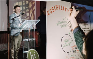 A speaker presents at an event promoting inclusive arts, while another person visually records ideas on a board. Words like “ACCESSIBILITY” and “New Strategies” emphasize collaboration, creativity, and advocacy for equal participation in cultural life.