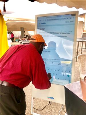 An African man wearing a longsleeves and a baseball cap using a life-sized electronic tablet to register for EnableMe forum.
