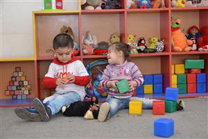 Two children are playing with colorful cubes in front of a toy shelf in Kindergarden in the Berd region.