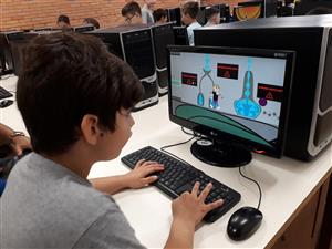 A young boy sits in front of the computer, while playing/testing a UNIVALI video game.